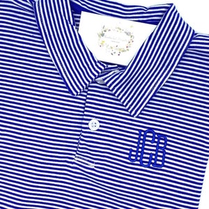 May include: A blue and white striped polo shirt featuring a classic collar, a single white button at the placket, and the embroidered monogram letters JCB in blue thread on the chest. A small white tag with floral graphics is tucked inside.