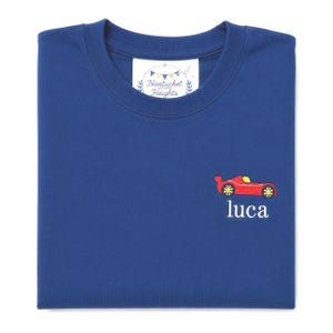 May include: A royal blue t-shirt featuring an embroidered red race car with yellow accents and the name "luca" stitched in white below it. The inner collar label displays the text "Nantucket Heights" with a small bunting graphic.