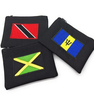 Puede incluir: Tres estuches negros con cremallera y banderas bordadas de Trinidad y Tobago, Barbados y Jamaica. La bandera de Trinidad y Tobago es roja con una franja negra. La bandera de Barbados es azul con un tridente amarillo.