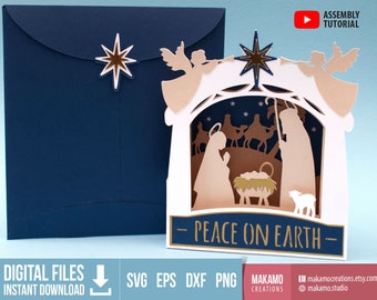 May include: A white papercraft card with a pop-up nativity scene. The scene features a stable with a manger, a star, angels, shepherds, and three wise men. The card has a blue background and the text "Peace on Earth" in gold lettering.