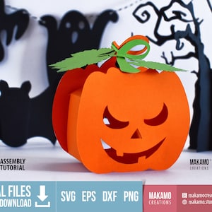 May include: A 3D papercraft pumpkin with a spooky face, green leaves, and a bow. The pumpkin is orange and has a black outline. The background is a white surface with black silhouettes of bats, ghosts, and trees.
