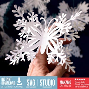 Pode incluir: Uma borboleta de papel branco com detalhes intrincados semelhantes a flocos de neve é segurada contra um fundo escuro. Outras borboletas semelhantes são visíveis no fundo. A imagem inclui o texto "SVG STUDIO" e "MAKAMO CREATIONS".