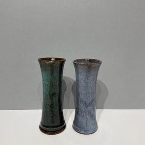 May include: Two ceramic vases, one green and one blue, with a brown glaze. The vases are tall and slender, with a rounded bottom and a flared top.
