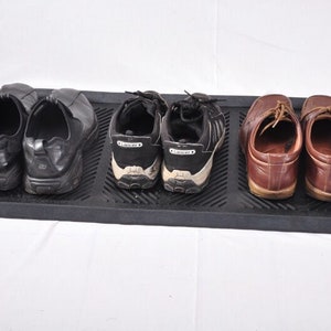 May include: A black rectangular shoe tray holds three pairs of shoes. The shoes include black leather slip-ons, black and white sneakers, and brown leather dress shoes with laces. The tray is made of a durable, textured material.