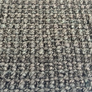 May include: Close-up of a dark brown woven rug with a textured surface. The rug is made of natural fibres and has a rustic look.