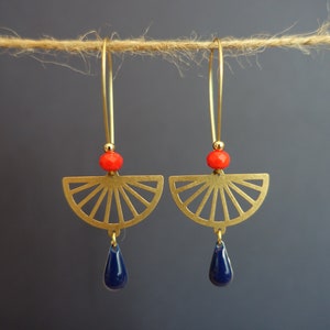May include: A pair of gold earrings with a fan-shaped design and a blue teardrop-shaped bead hanging from each. The earrings have a red bead at the top of the fan.