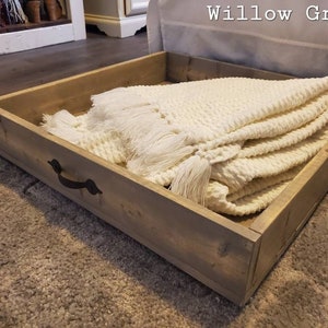 May include: A wooden storage box with a white blanket inside. The box has a metal handle and is labeled "Willow Gray".
