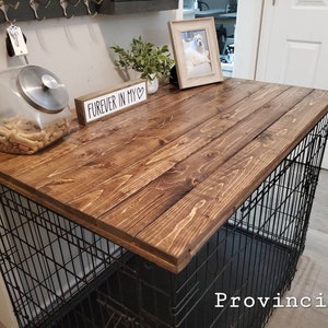 Pu&ograve; includere: Un piano d'appoggio in legno tinto marrone scuro progettato per adattarsi sopra una gabbia per cani in filo metallico nero. Il piano rettangolare in legno presenta una venatura visibile ed &egrave; posizionato orizzontalmente come superficie.