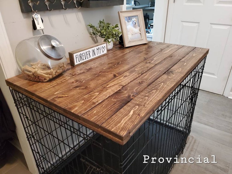 Pu&ograve; includere: Un piano d'appoggio in legno tinto marrone scuro progettato per adattarsi sopra una gabbia per cani in filo metallico nero. Il piano rettangolare in legno presenta una venatura visibile ed &egrave; posizionato orizzontalmente come superficie.