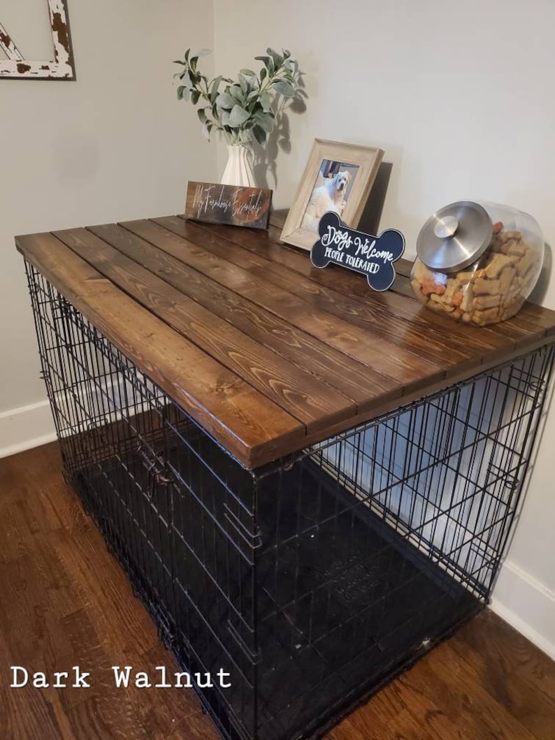 May include: A dark walnut dog crate with a wooden top. The crate has a black metal frame and a black plastic tray. The top is decorated with a framed photo, a bone-shaped sign that says "Dogs Welcome People Tolerated", and a glass jar of dog treats.