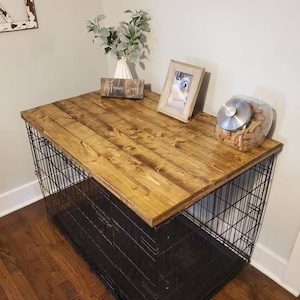 May include: A dog crate with a stained wooden top, featuring a black wire cage base. The top is decorated with a framed photo, a vase with greenery, and a jar of dog treats. The words "Early American" are in the background.