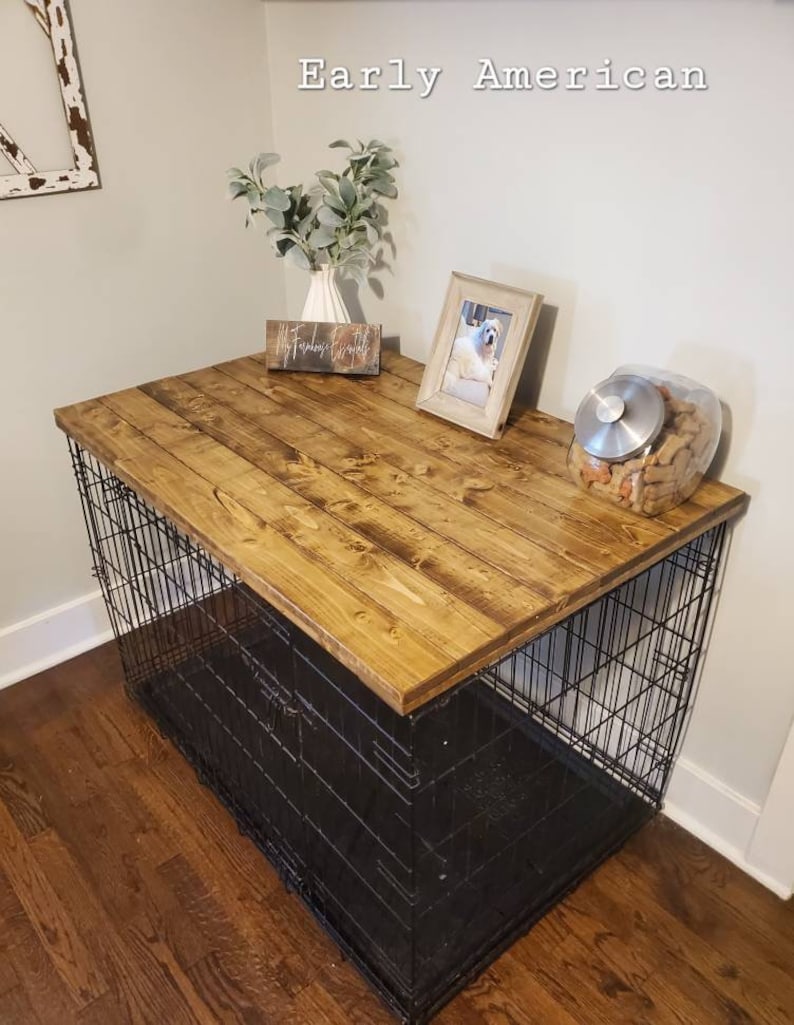 May include: A dog crate with a stained wooden top, featuring a black wire cage base. The top is decorated with a framed photo, a vase with greenery, and a jar of dog treats. The words "Early American" are in the background.