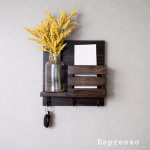 May include: A dark espresso-stained wooden wall organizer with a shelf, mail slots, and key hooks. A clear glass vase holds yellow decorative stems. A white card is in the mail slot, and keys hang from the hooks. The word "Espresso" is at the bottom.
