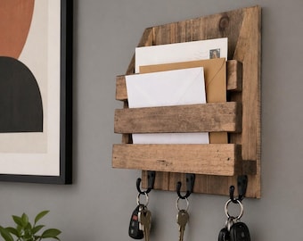 May include: A wall-mounted wooden mail organizer with a natural brown finish, featuring three horizontal slats to hold envelopes and three black metal hooks underneath, each holding a set of metal keys and key fobs.