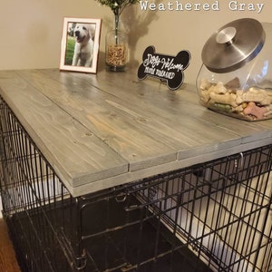 Pu&ograve; includere: Un coperchio per gabbia in legno grigio invecchiato con un design a doghe rettangolari. La superficie superiore &egrave; liscia e poggia su una gabbia per cani in filo metallico nero. Il testo Weathered Gray &egrave; visibile in alto a destra.
