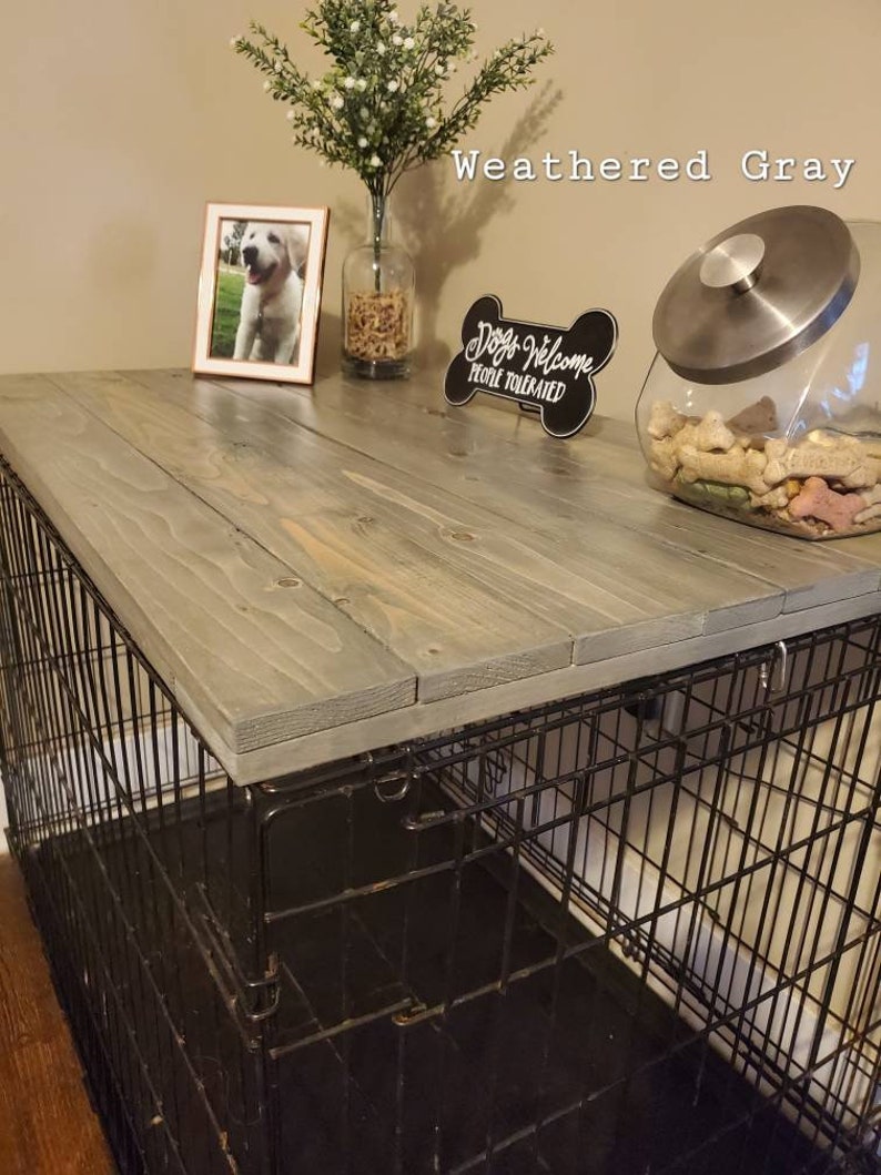 Pu&ograve; includere: Un coperchio per gabbia in legno grigio invecchiato con un design a doghe rettangolari. La superficie superiore &egrave; liscia e poggia su una gabbia per cani in filo metallico nero. Il testo Weathered Gray &egrave; visibile in alto a destra.