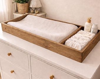 May include: A wooden changing table topper with a white changing pad and a section for diapers and baby products. The topper sits on a white dresser with gold knobs. The text "Special Walnut" is at the bottom.
