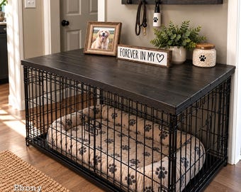 May include: A black metal dog crate with a dark wood top surface. Inside the crate is a beige pet bed with a black paw print pattern. On the wooden top sits a framed photo of a dog, a sign reading "FOREVER IN MY ♡", a potted plant, and a jar.