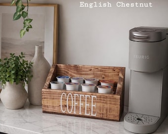 May include: A wooden coffee pod holder with the word "COFFEE" in white lettering. The holder is filled with coffee pods and sits next to a gray coffee maker. The text "English Chestnut" is above the holder.
