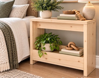 May include: A rectangular natural pine console table featuring a flat top surface and a lower shelf. The table has a light wood grain finish and is styled with a potted green plant, stacked books, a wooden bowl, and a decorative wooden chain link.