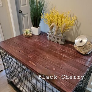 Pu&ograve; includere: Una copertura in legno marrone scuro per gabbia per cani con finitura liscia e venature del legno visibili, con il testo Black Cherry stampato sulla superficie. La parte superiore &egrave; piatta e rettangolare, usata come piano per piante.