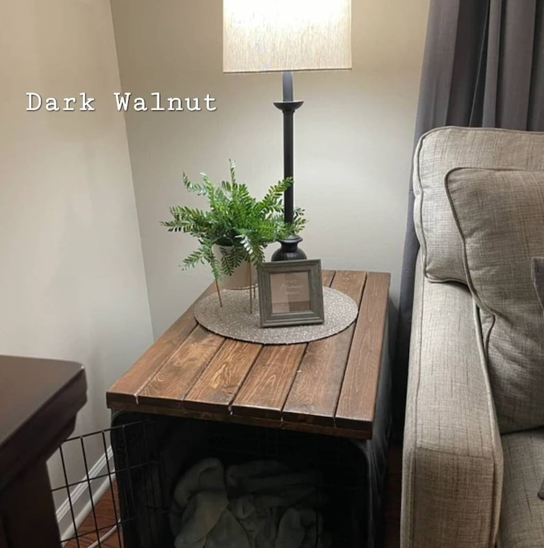 Pu&ograve; includere: Una copertura per gabbia in legno di noce scuro con superficie a doghe. Il testo Dark Walnut &egrave; visibile in alto a sinistra. Una lampada, una pianta verde in vaso e una piccola cornice quadrata poggiano sulla superficie in legno.