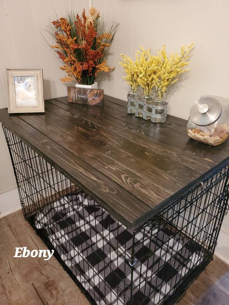 May include: A dark stained wooden dog crate with a black wire frame. The crate has a black and white plaid blanket inside. The top of the crate is decorated with fall-themed floral arrangements, a framed photo, and a jar of dog treats. The word "Ebony" is visible.