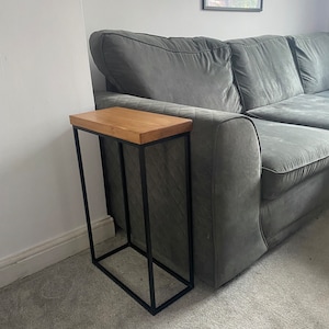 May include: A black metal side table with a wooden top. The table is next to a grey sofa.