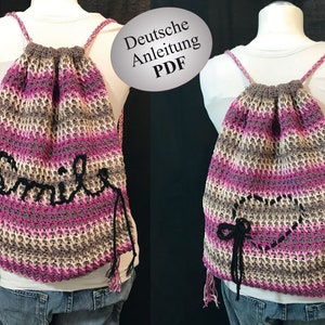 Könnte beinhalten: Eine rosa und braune gehäkelte Kordeltasche mit schwarzen Trägern. Die Tasche hat ein schwarzes gehäkeltes "Smile" auf der Vorderseite und ein schwarzes gehäkeltes Herz auf der Rückseite.
