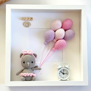 May include: A white picture frame with a crocheted teddy bear holding pink and purple balloons. The frame also includes a small wooden clock and wooden blocks spelling "LISA".
