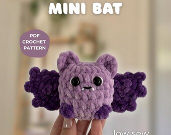 May include: A handmade, plush, purple crochet bat with dark purple wings and accents. The bat has small black eyes and a tiny mouth. Text on the image reads "MINI BAT", "PDF CROCHET PATTERN", and "low sew".