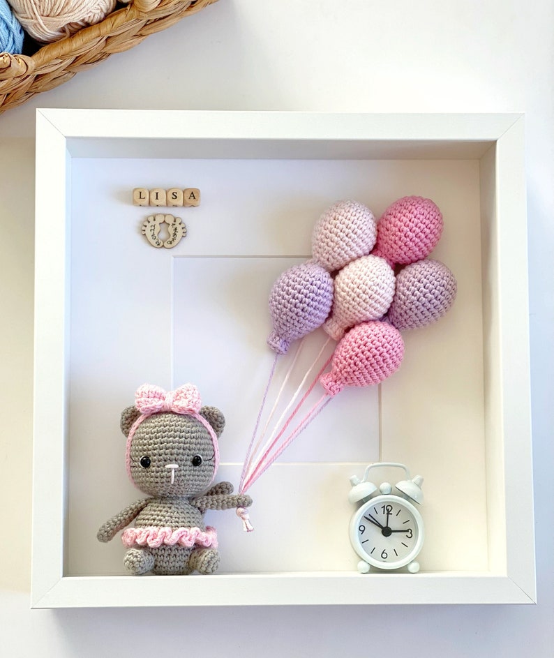 May include: A white picture frame with a crocheted teddy bear holding pink and purple balloons. The frame also includes a small wooden clock and wooden blocks spelling "LISA".