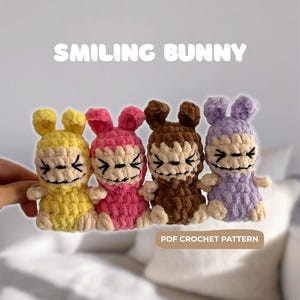 May include: Four smiling bunny crochet dolls in yellow, pink, brown, and purple. Each bunny has a smiling face with black embroidered details. The text "SMILING BUNNY" is above the dolls, and "PDF CROCHET PATTERN" is below.