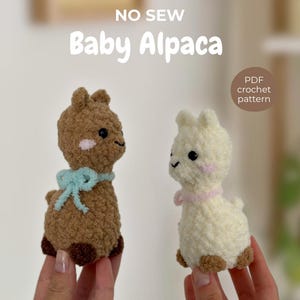 May include: Two crocheted baby alpaca figures, one brown with a light blue bow and one cream with a pink collar. Both have dark eyes and pink cheeks. Text reads: NO SEW Baby Alpaca and PDF crochet pattern. The figures are made of textured yarn.