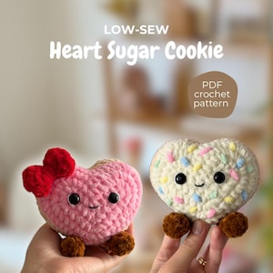 Puede incluir: Dos peluches de ganchillo en forma de corazón, uno rosa con un lazo rojo y otro blanco con chispas de colores. Ambos tienen ojos negros y pies marrones. El texto dice "LOW-SEW Heart Sugar Cookie" y "PDF crochet pattern".