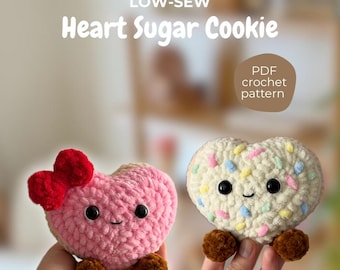 May include: Two heart-shaped crochet plushies, one pink with a red bow and the other white with colorful sprinkles. Both have black eyes and brown feet. Text reads "LOW-SEW Heart Sugar Cookie" and "PDF crochet pattern".