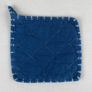 May include: A blue quilted cotton hot pad with a white stitched border. The hot pad has a diamond pattern and a loop handle.