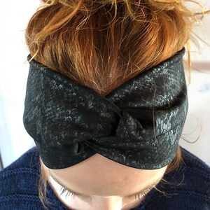 Könnte beinhalten: Ein schwarzes und graues gemustertes Stirnband mit einem gedrehten Knotendesign.