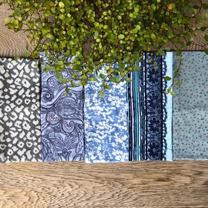Könnte beinhalten: Eine Sammlung von acht Stoffmustern in verschiedenen Mustern und Farben, darunter florale, Paisley- und geometrische Designs. Die Muster sind horizontal auf einer Holzoberfläche angeordnet.