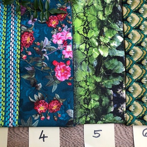 May include: Four fabric swatches with numbers 3, 4, 5, and 6 written on sticky notes below them. The swatches are all different patterns: a blue and green striped pattern, a blue floral pattern, a green snake skin pattern, and a green and gold geometric pattern.