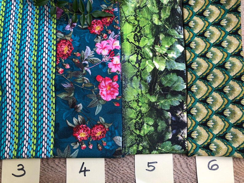 May include: Four fabric swatches with numbers 3, 4, 5, and 6 written on sticky notes below them. The swatches are all different patterns: a blue and green striped pattern, a blue floral pattern, a green snake skin pattern, and a green and gold geometric pattern.