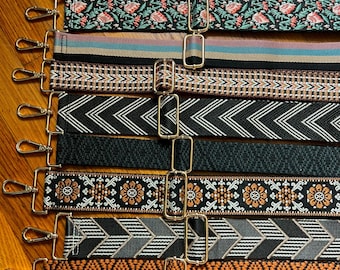 Puede incluir: Una colección de nueve correas ajustables para bolsos con diversos patrones tejidos, incluyendo motivos florales, rayas en zigzag, formas geométricas y bandas sólidas. Cada correa cuenta con ganchos giratorios y hebillas deslizantes de metal dorado.