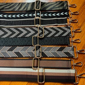 Puede incluir: Una colección de siete correas ajustables para bolsos con varios patrones, incluyendo estampado de cebra, chevrons geométricos, motivos de grecas y rayas sólidas en negro, marrón, gris y blanco, con ganchos giratorios de metal dorado.
