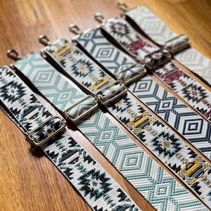 May include: A collection of woven bag straps with various geometric patterns. The straps feature a mix of colors, including teal, gray, yellow, and burgundy, with gold-colored metal hardware. The designs include diamond, Aztec, and other geometric shapes.