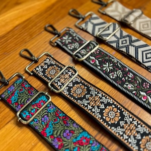 May include: Five different colourful woven straps with gold metal clasps. The straps are black with various colourful floral patterns.