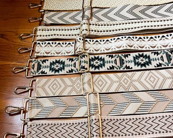 May include: A collection of eight adjustable bag straps featuring various woven patterns in neutral tones of beige, cream, white, and dark green. Each strap is equipped with gold-toned metal hardware, including swivel lobster clasps and sliders.