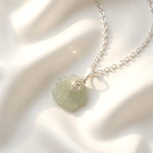 Op de afbeelding: Een lichtgroene, uit steen gesneden bloemhanger aan een fijne, zilverkleurige metalen ketting. De hanger heeft een bloemmotief met vijf bloemblaadjes, bevestigd aan de ketting met een eenvoudige, met de hand gewikkelde zilveren draadlus.