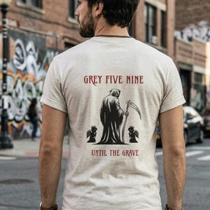 May include: A light grey t-shirt with the text "GREY FIVE NINE" above a Grim Reaper graphic holding a scythe, with the text "UNTIL THE GRAVE" below. The shirt is worn by a person in a city setting.