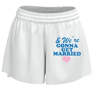 May include: White athletic shorts with an elastic waistband. The shorts feature the text "& We're Gonna Get Married" in blue, with a pink heart below the text. The shorts are made of a soft, lightweight material.