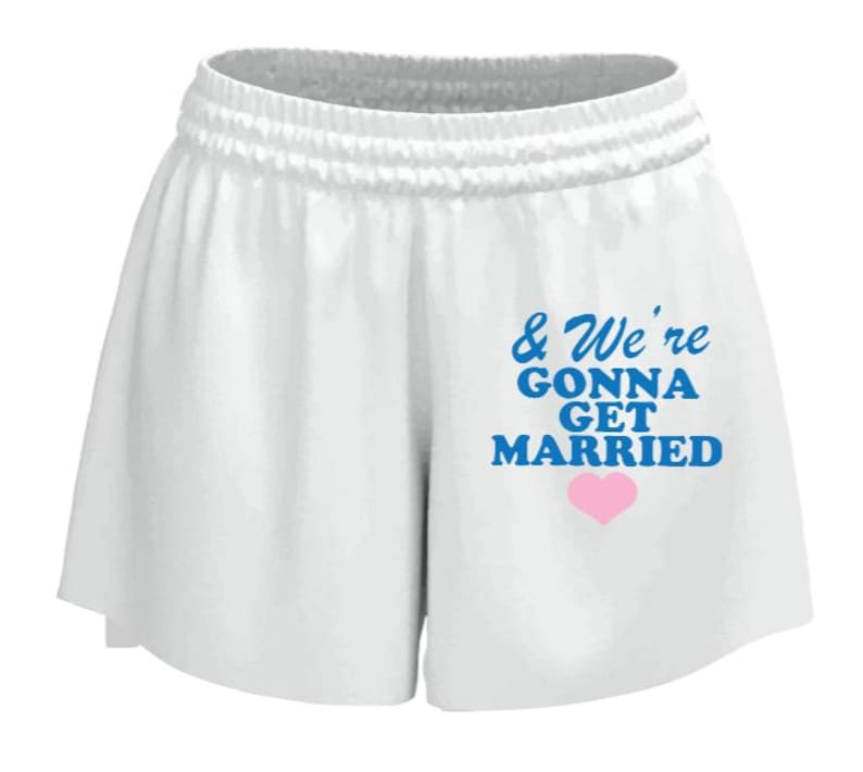 May include: White athletic shorts with an elastic waistband. The shorts feature the text "& We're Gonna Get Married" in blue, with a pink heart below the text. The shorts are made of a soft, lightweight material.